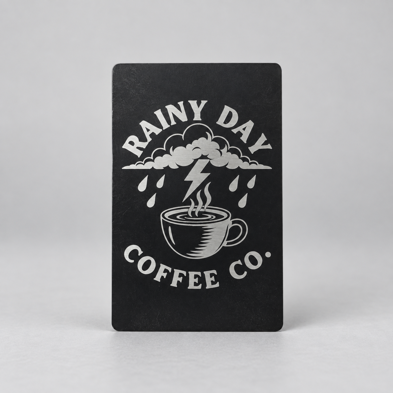 Black metal card engraved with a Rainy Day Coffee Co. coffee and storm design
